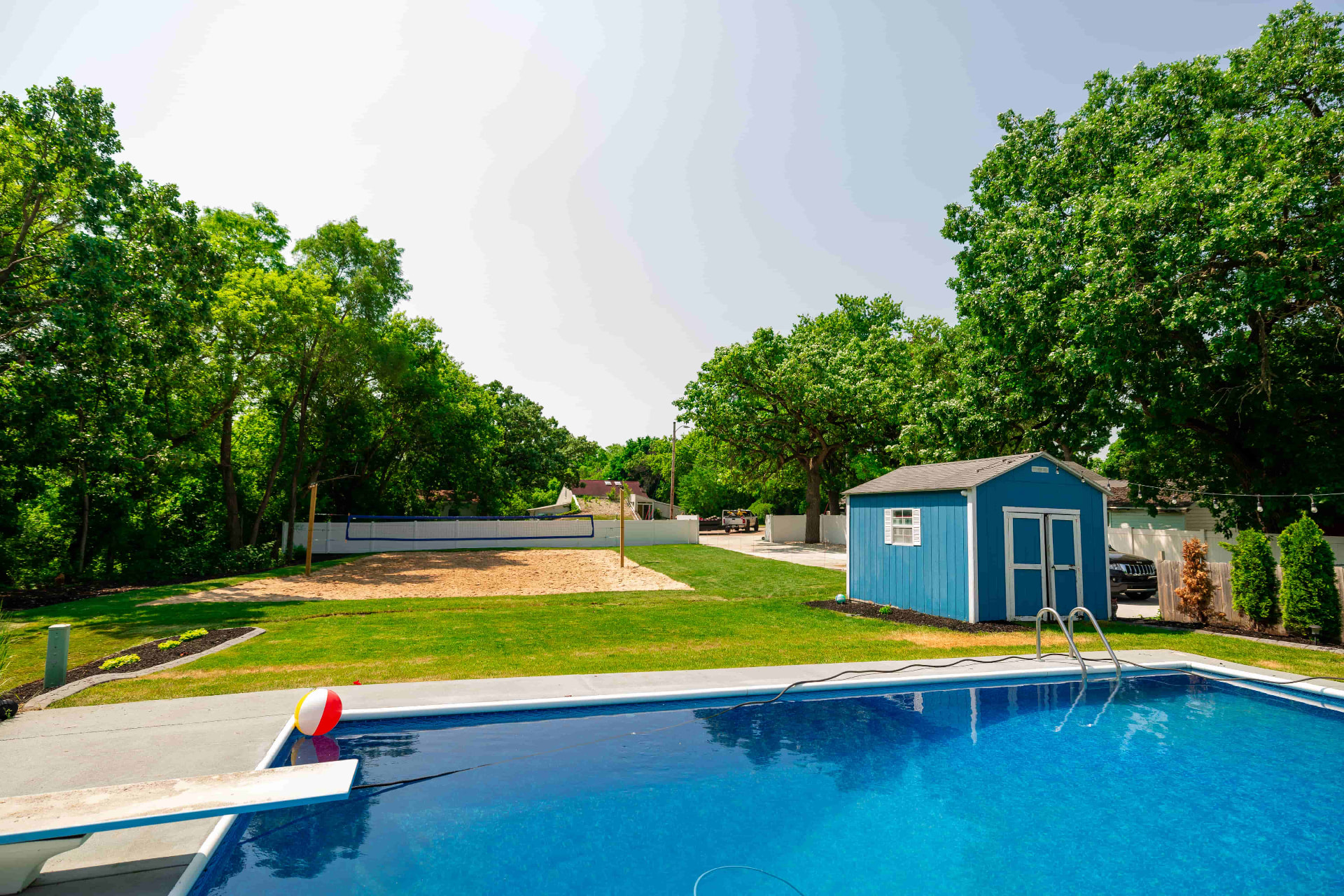 Backyard with in-ground pool, sand volleyball court, mowed lawn, and blue shed